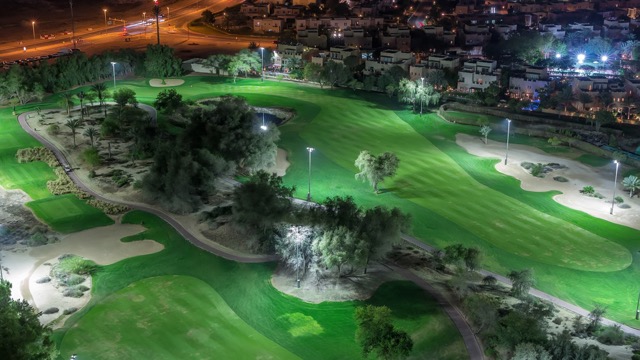 Aerial view to Golf course and villas with houses night timelapse. Illuminated lawn. Lakes with fountains