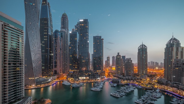 Dubai marina tallest skyscrapers and yachts in harbor aerial night to day transition during sunrise. View at apartment buildings, hotels and office blocks, modern residential development of UAE